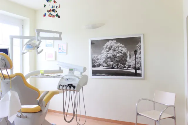 Zweites Behandlungszimmer mit gelb-grauem Behandlungsstuhl und großem Schwarz-Weiß-Foto an der Wand