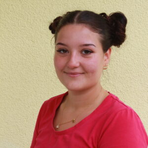 Freundliche junge Frau mit braunem Haar mit Pferdeschwanz und Nasenring und pinkfarbenen T-Shirt.