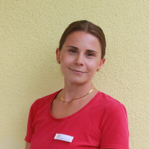 Freundliche junge Frau mit braunem Haar mit Pferdeschwanz und pinkfarbenen T-Shirt.