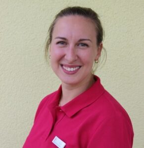 Freundliche junge Frau mit braunem Haar mit Pferdeschwanz und Nasenring und pinkfarbenen T-Shirt.